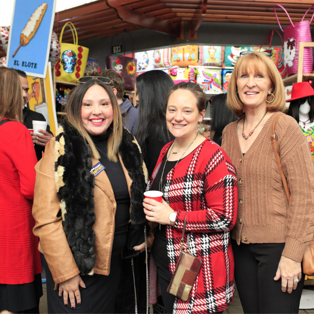 In the boutique there are three women shopping for multicultural and handmade products. The women are dressed in fall outfits and one of them is holding a cup of coffee