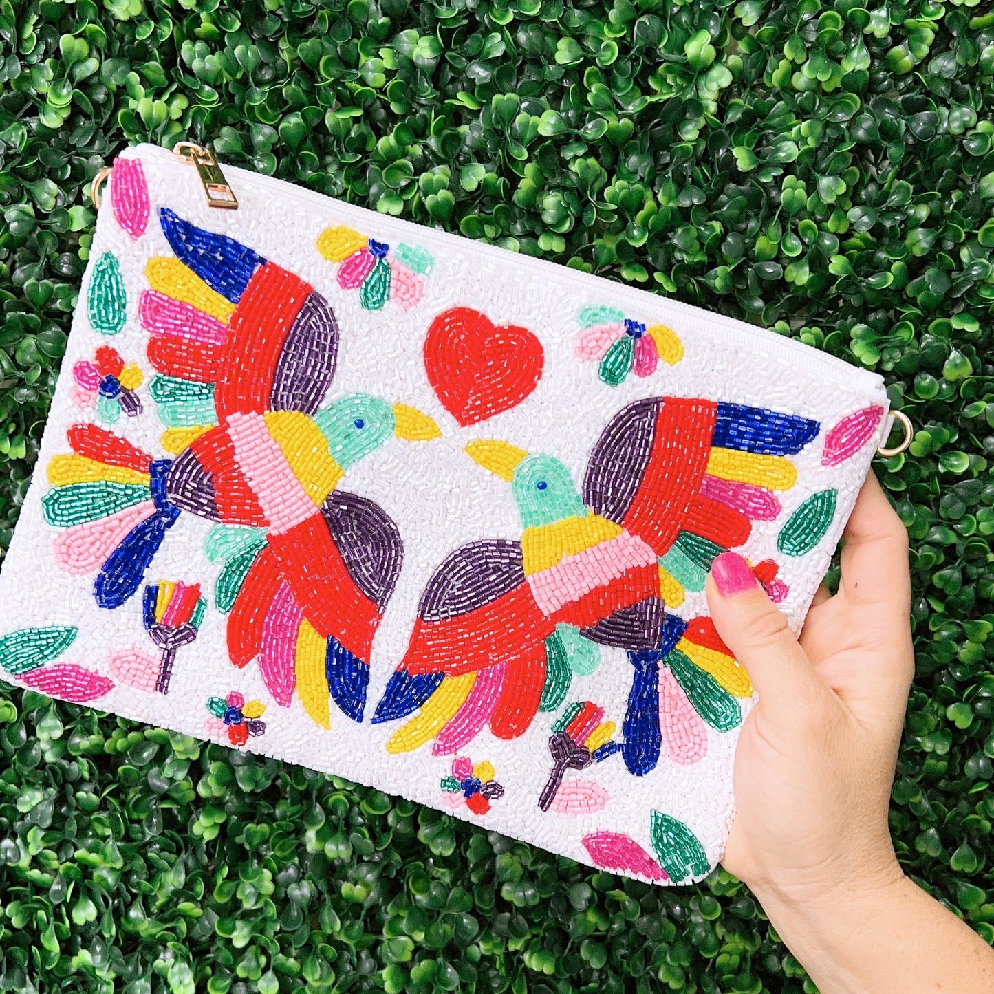 The colorful beaded handbag is made with intricate beading. The bag has two birds with different colors, in the center is a red heart and the bag is white in color.