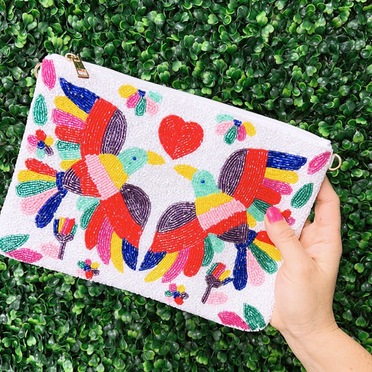 The colorful beaded handbag is made with intricate beading. The bag has two birds with different colors, in the center is a red heart and the bag is white in color.