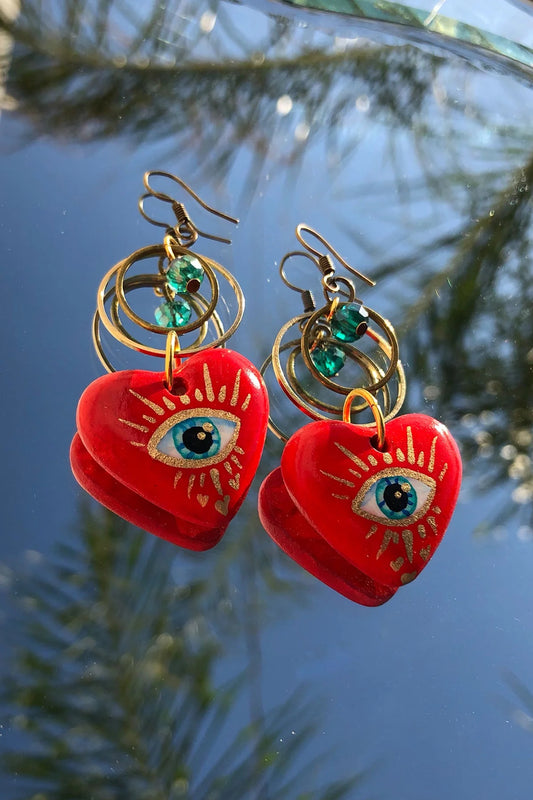 Multicultural red earrings hand painted by artisans. They are heart shaped and have a gold eye with silver plated in the center.