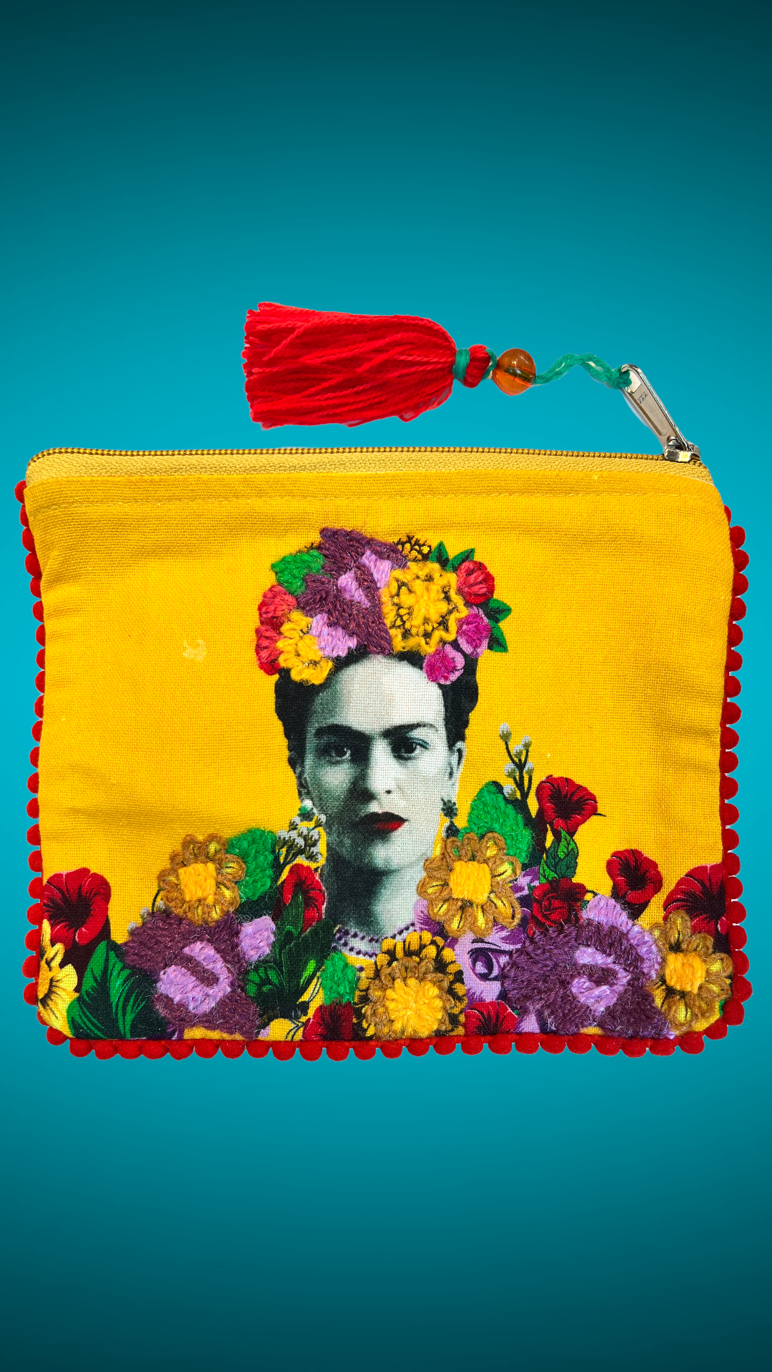 Yellow embroidered purse design with the image of Frida Kahlo in the center with purple and blue flowers. The zipper has a red pom pom as a detail.