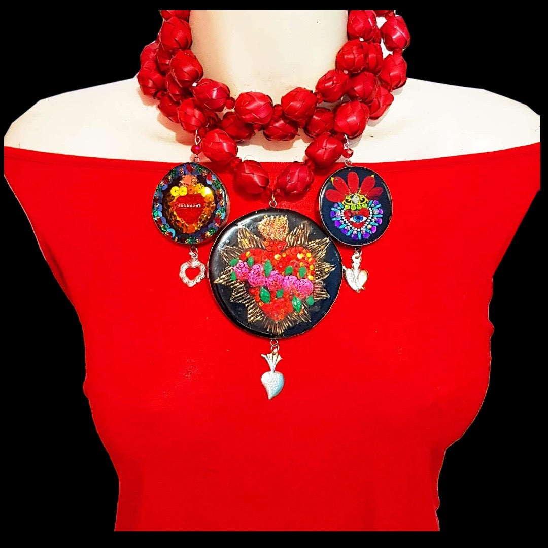 Medallones Choker necklaces with three circular charms of different sizes and hand painted with red Mexican hearts. The necklace is designed with red paper mache with small hanging elements.