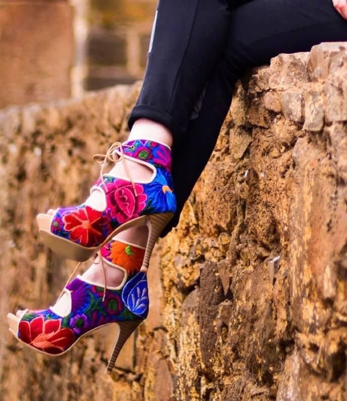 High heels with blue, red and yellow floral embroidery. A woman uses de heels and is dressed with black jean