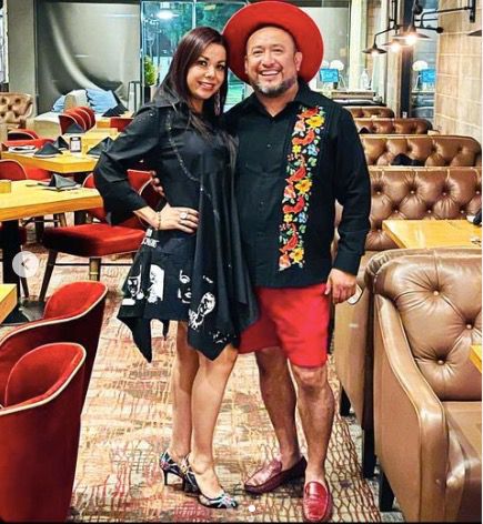 The founder of the multicultural store is dressed in an outfit that represents the brand with a handmade red hat, a black shirt with embroidered flowers in different colors. The woman is wearing a black dress with white 