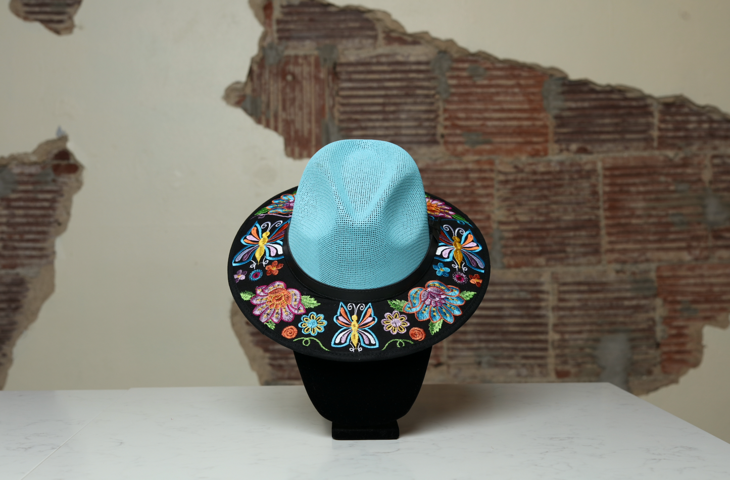 Hand embroidered blue brim hat, the perfect accessory to add fun and style to any outfit. With black, purple and blue flowers and butterflies as multicultural embellishments.