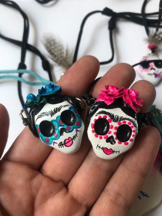 Two pink and blue handmade paper mache catrinas necklaces inspired by the traditional Mexican Day of the Dead celebrations.