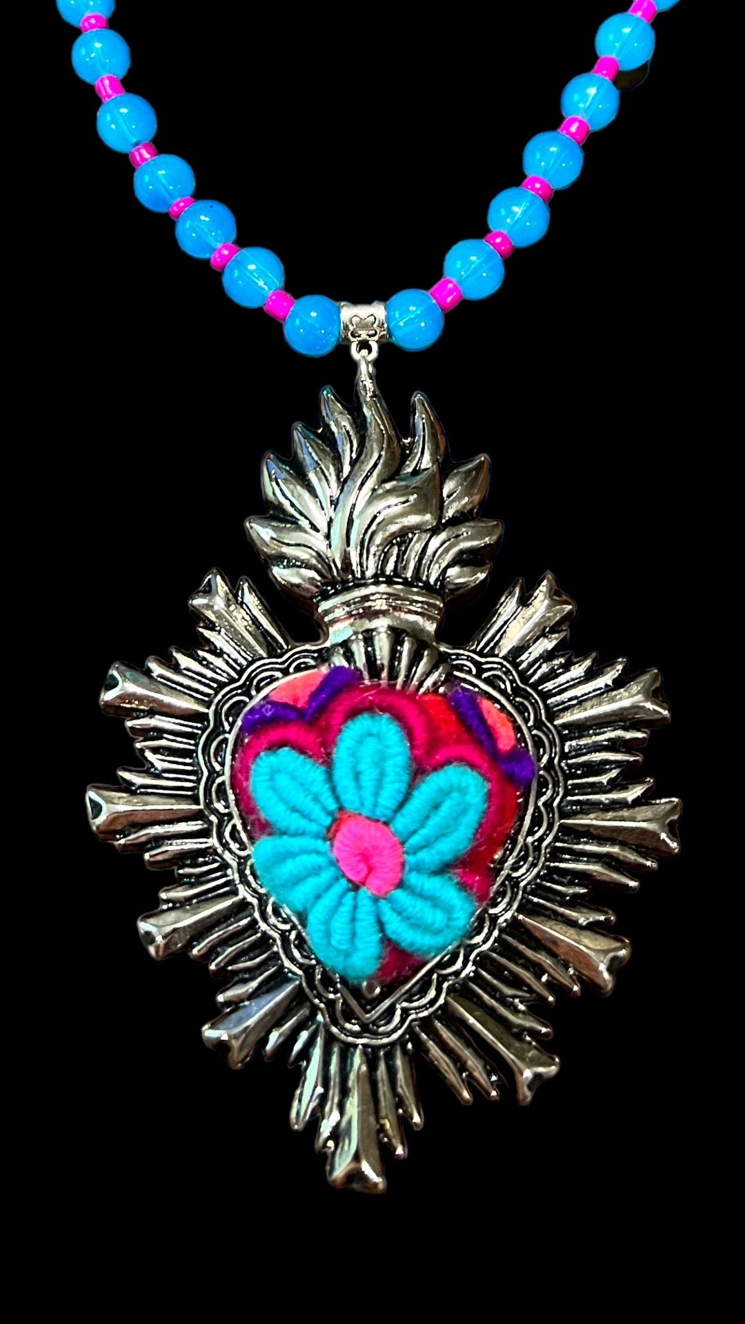 Cultural fashion necklace of red, blue, pink and purple hearts. In the center it has a handmade blue flower and around it has silver ornaments, and the chain is made with blue and pink stones.