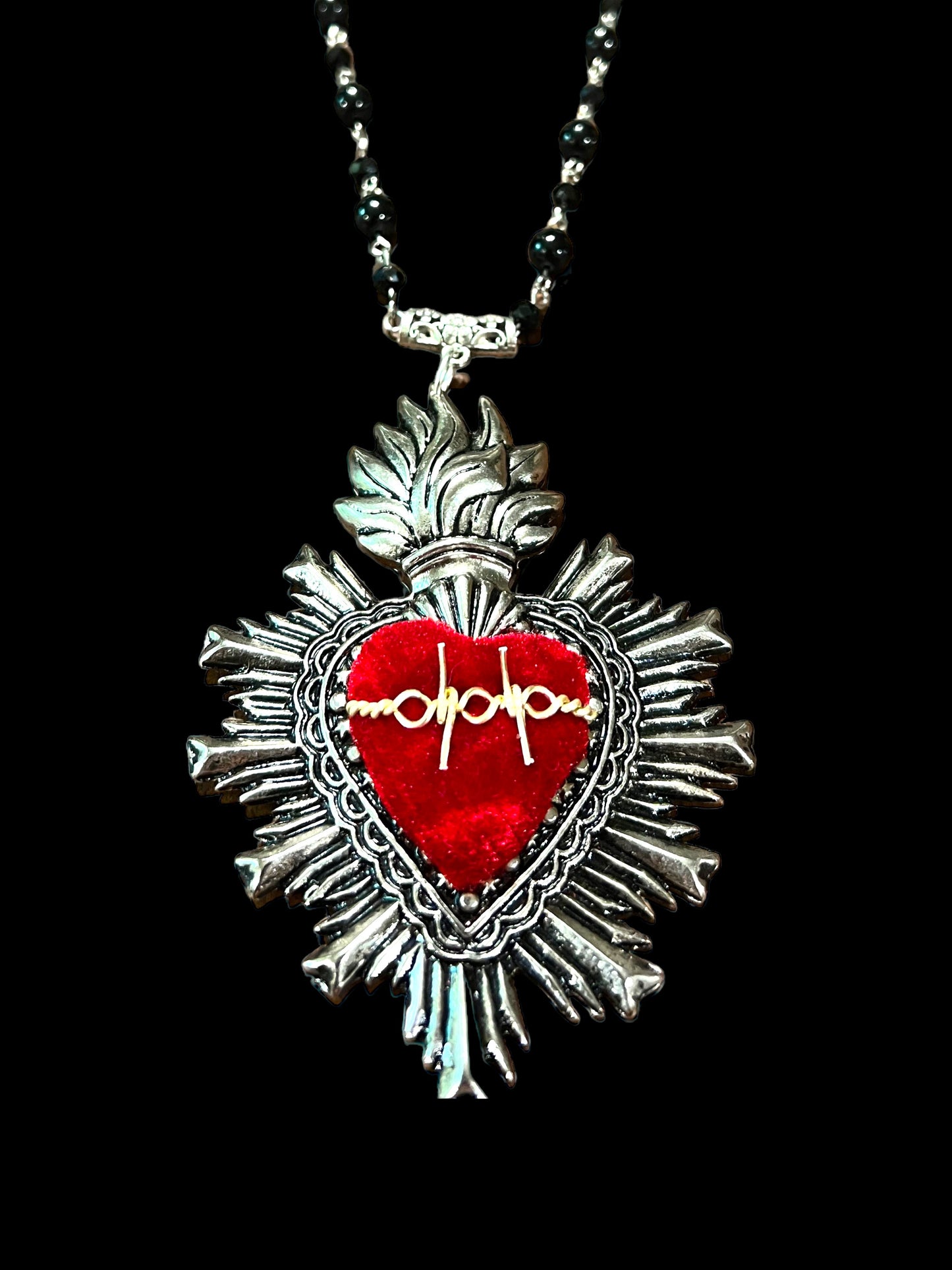 Red and silver cultural fashion necklace. the center is red and has a golden ornament, the chain is made with black and silver stones.