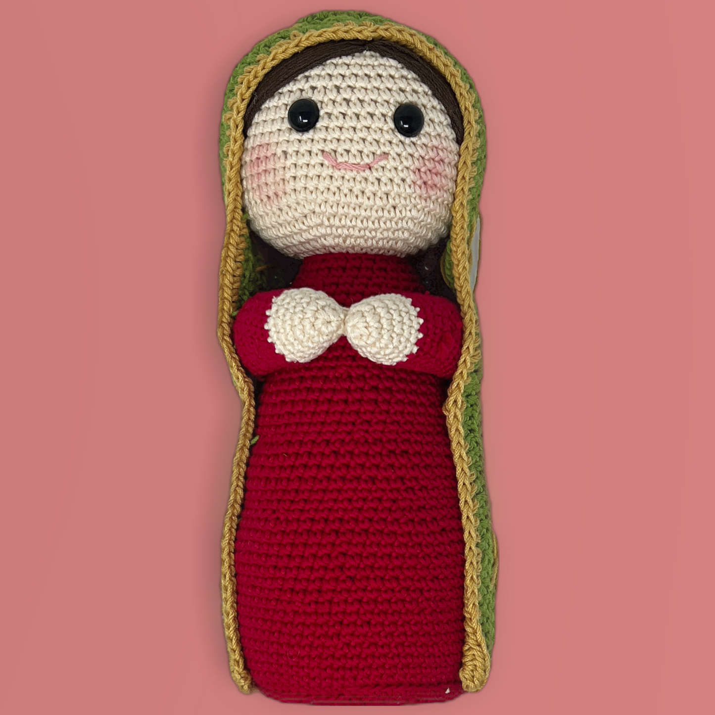 Handmade crochet dolls and is made with red dress and green manta. the doll's eye are open and is in a pink background and crafted by hand