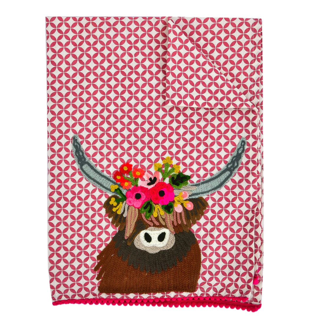 Embroidered towel with a longhorn in the center and decorated with a wreath of flowers on the head. The hand-designed towel has white textures with red, and on the border there are small pompoms.